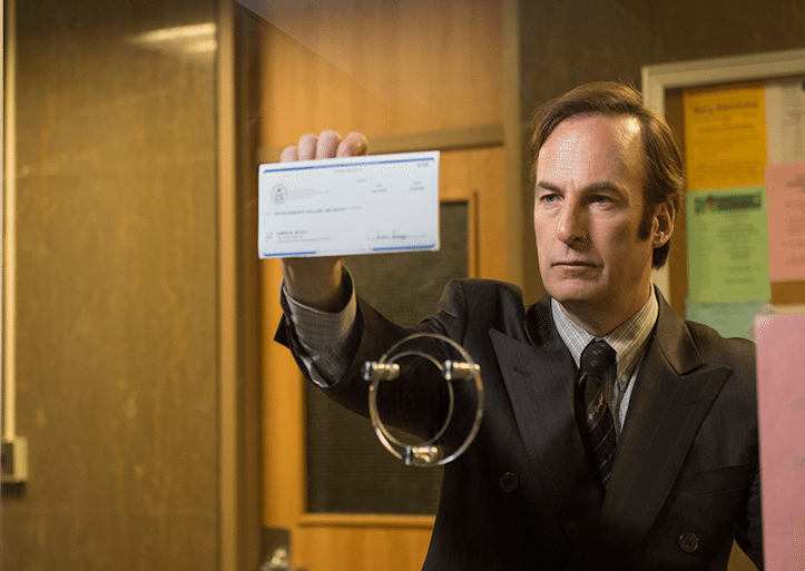 A man in a suit holding up a check for Better Call Saul.