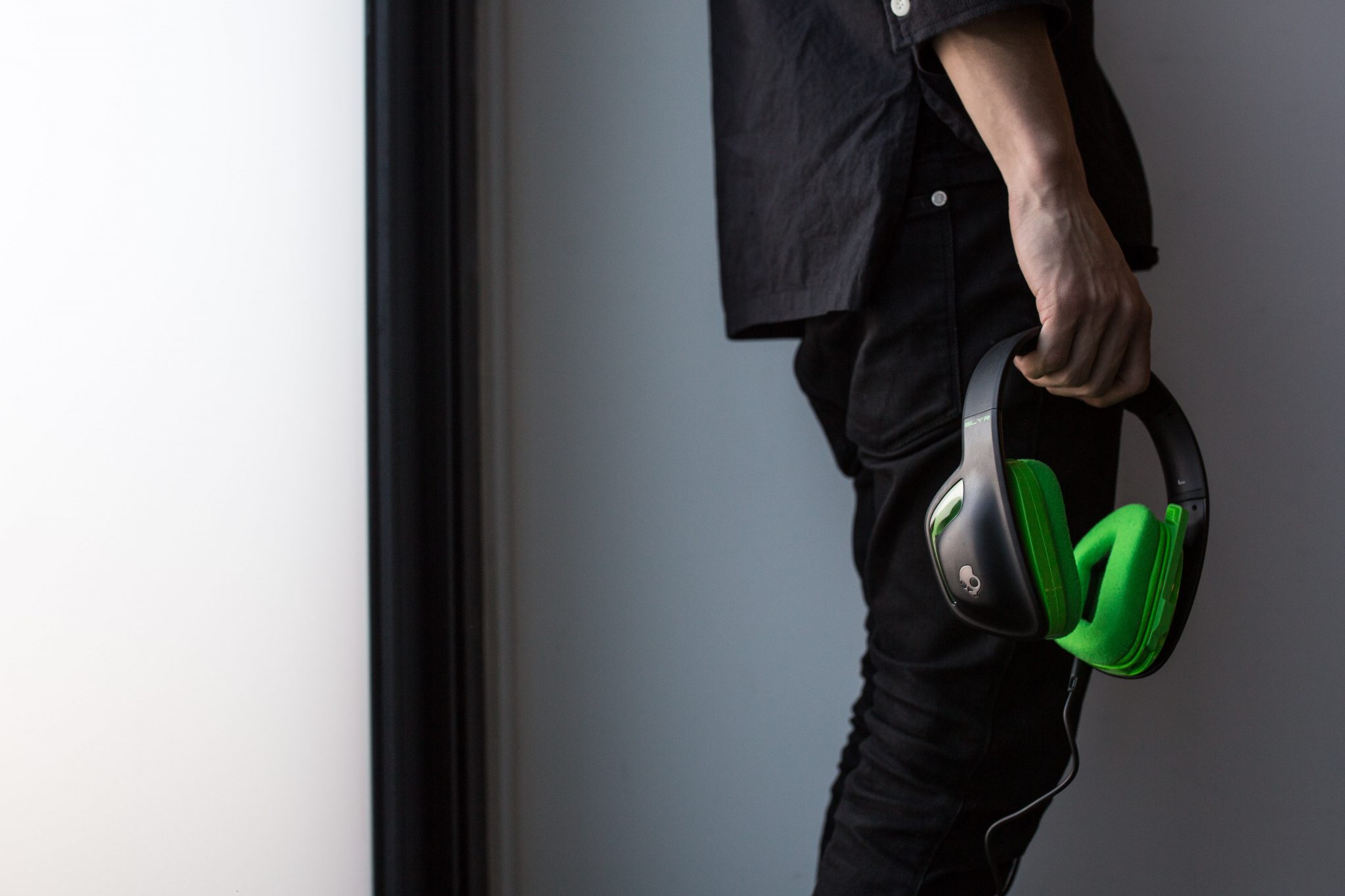H1A7536 Skullcandy Releases Astro Designed SLYR Headset For Xbox One A man wearing Skullcandy green headphones is standing in front of a door.