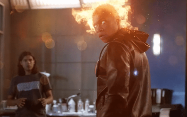 A man in a black jacket is standing in front of a firestorm.