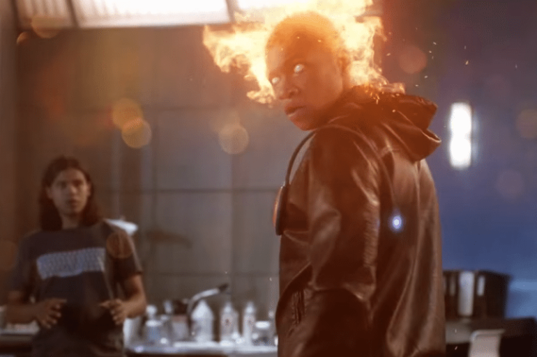 A man in a black jacket is standing in front of a firestorm.