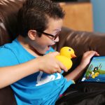 A young boy playing with Edwin The Duck on a couch.