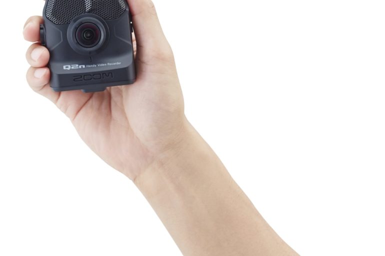 A person holding up a small Q2n camera on a white background.