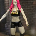 A pink haired action figure from Mattel is standing in front of a brick wall.