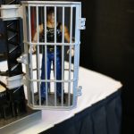 A Mattel figure in a cage on a table.