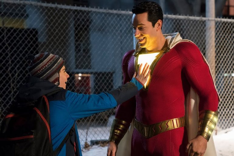 At SDCC 2018, a young boy excitedly holds up a Shazam costume in front of a fence during the Teaser Trailer release.