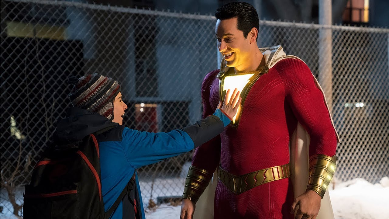 At SDCC 2018, a young boy excitedly holds up a Shazam costume in front of a fence during the Teaser Trailer release.