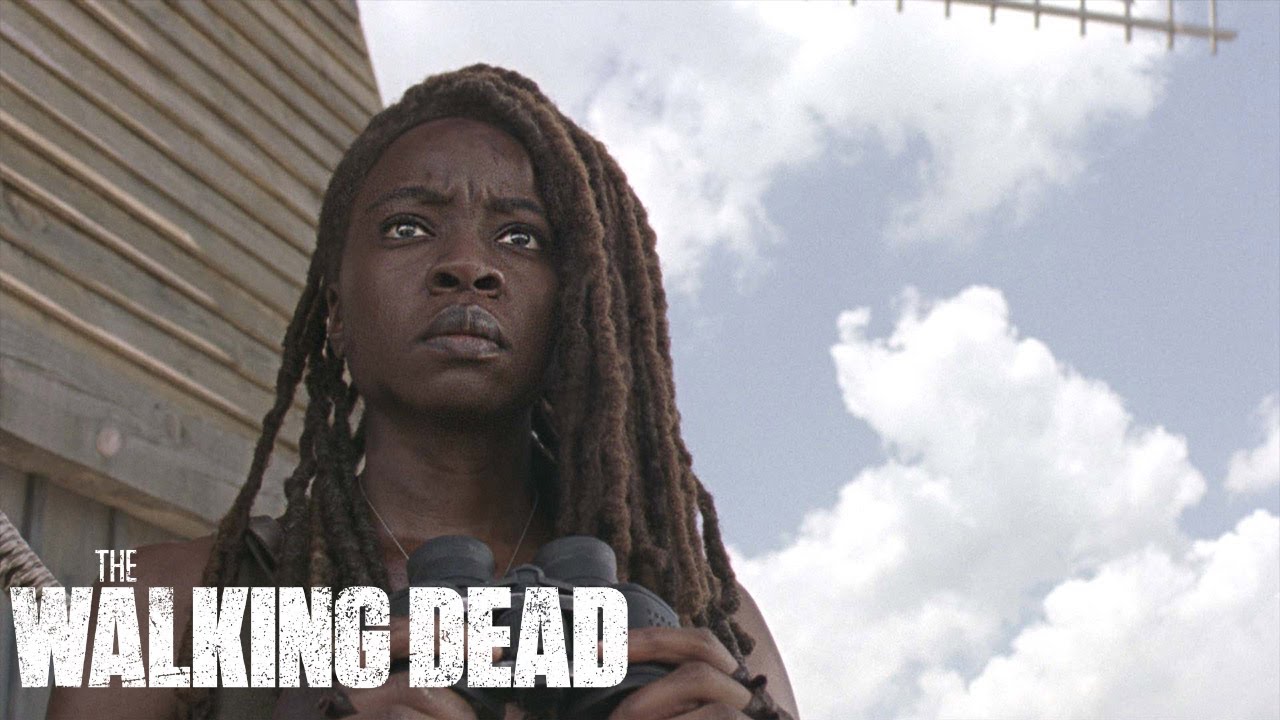 The Walking Dead Season 10 - a woman with dreadlocks in front of a building.