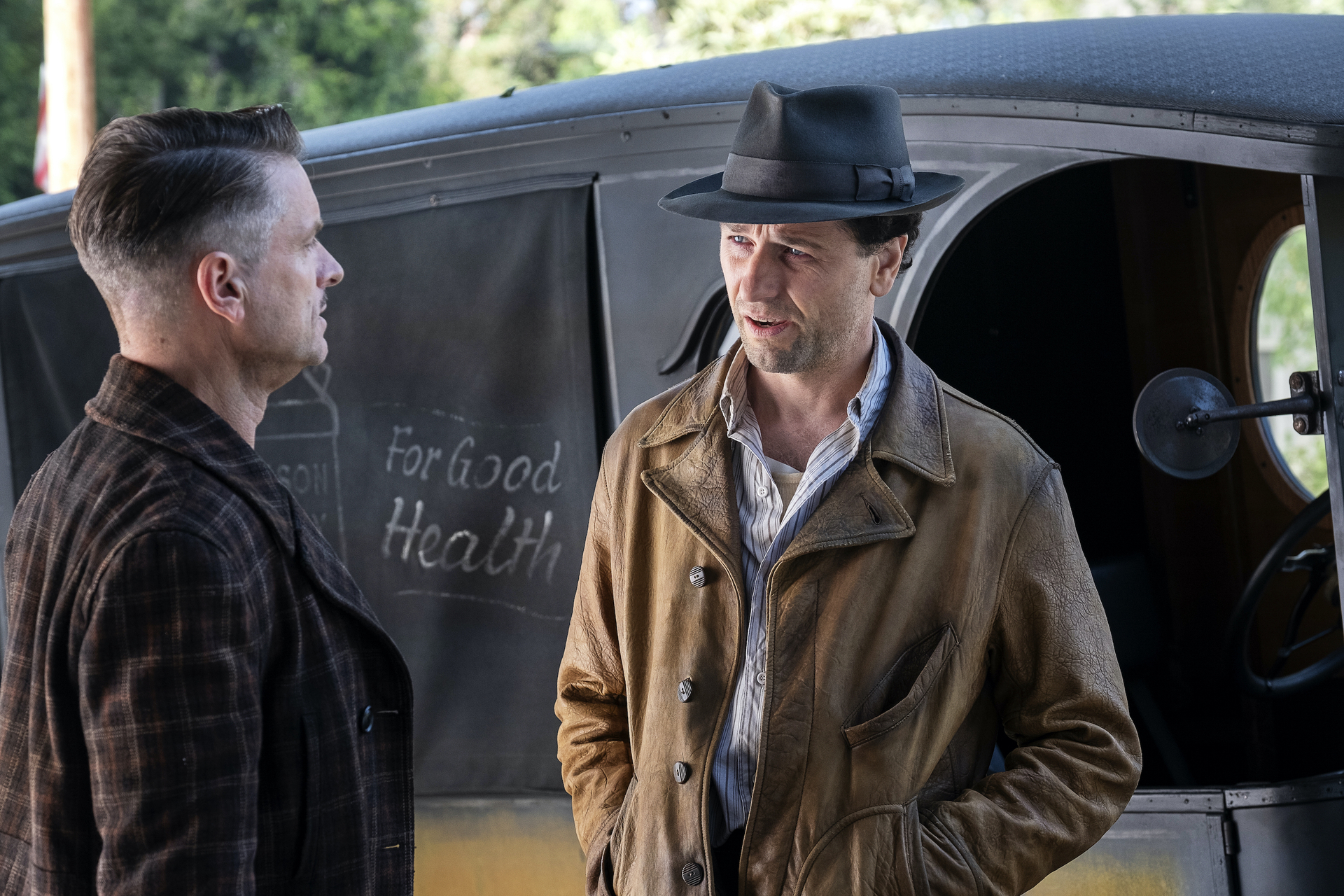 Two men in hats standing next to an Official Trailer truck.