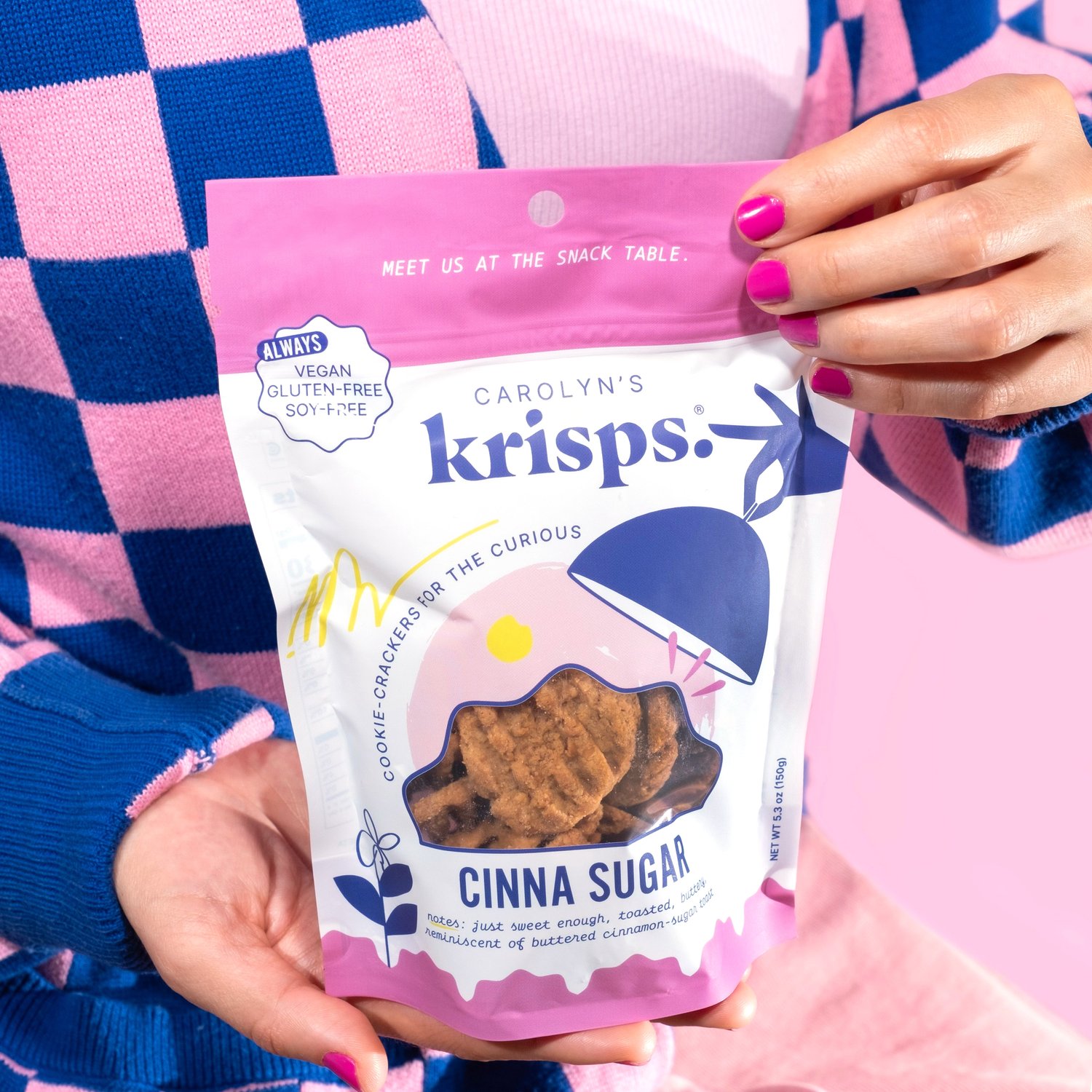 A person holding a bag of Carolyn's Krisps Cinna Sugar cookie crackers. Perfect for those seeking vegan, gluten-free, and soy-free options, these treats make an ideal treat featured in the RAGE Works holiday food gift guide. 