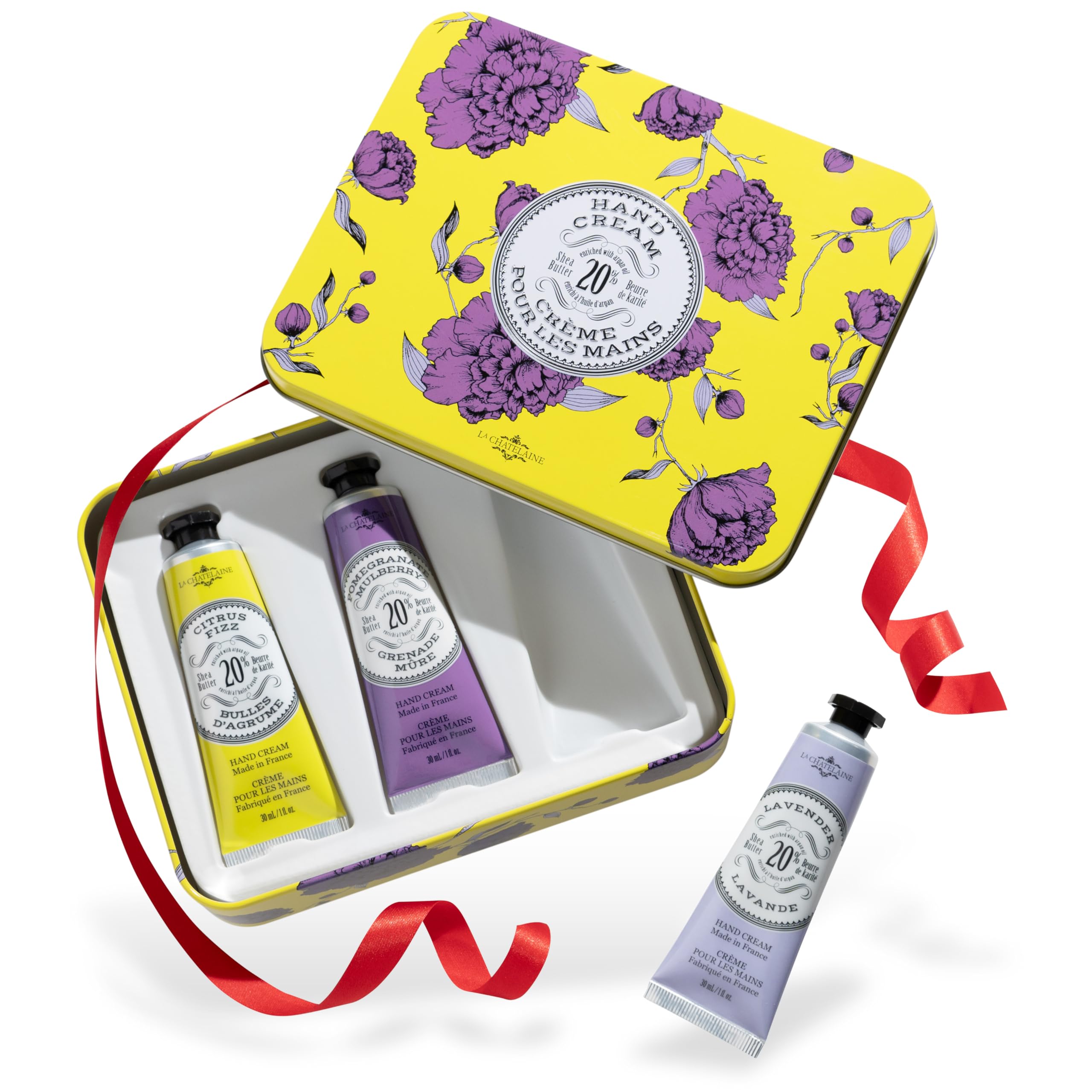 This charming tin box, perfect for the Holiday Gift Guide, features purple flowers on a sunny yellow background and holds three hand cream tubes in pink, purple, and lavender. A festive red ribbon adds a delightful finishing touch.