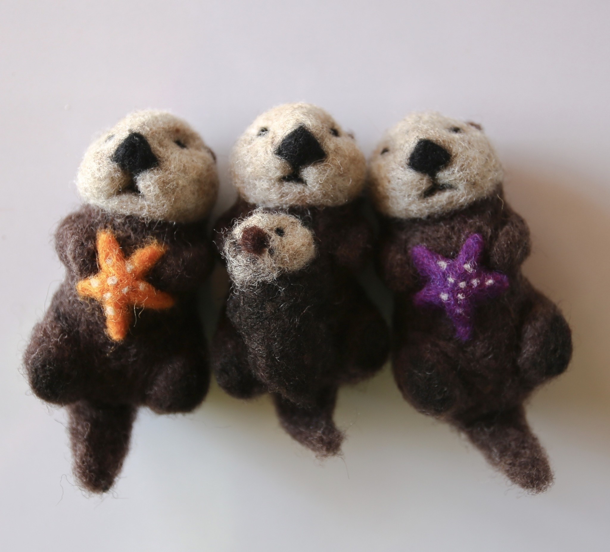 In our Holiday Gift Guide, discover three felt otters lying side by side, lovingly clutching starfish—a charming addition to any collection.